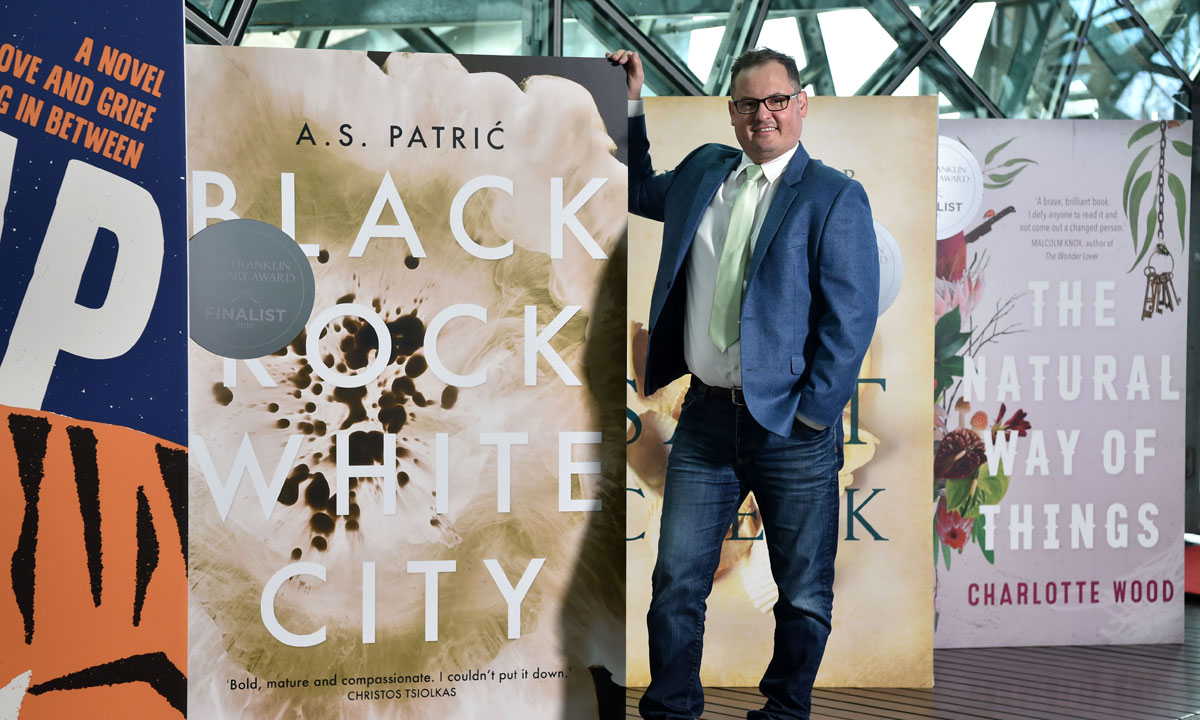 Alec Patric with a large image of the cover of his book alongside those of previous Mile Franklin Literary Award winners. Photo: supplied