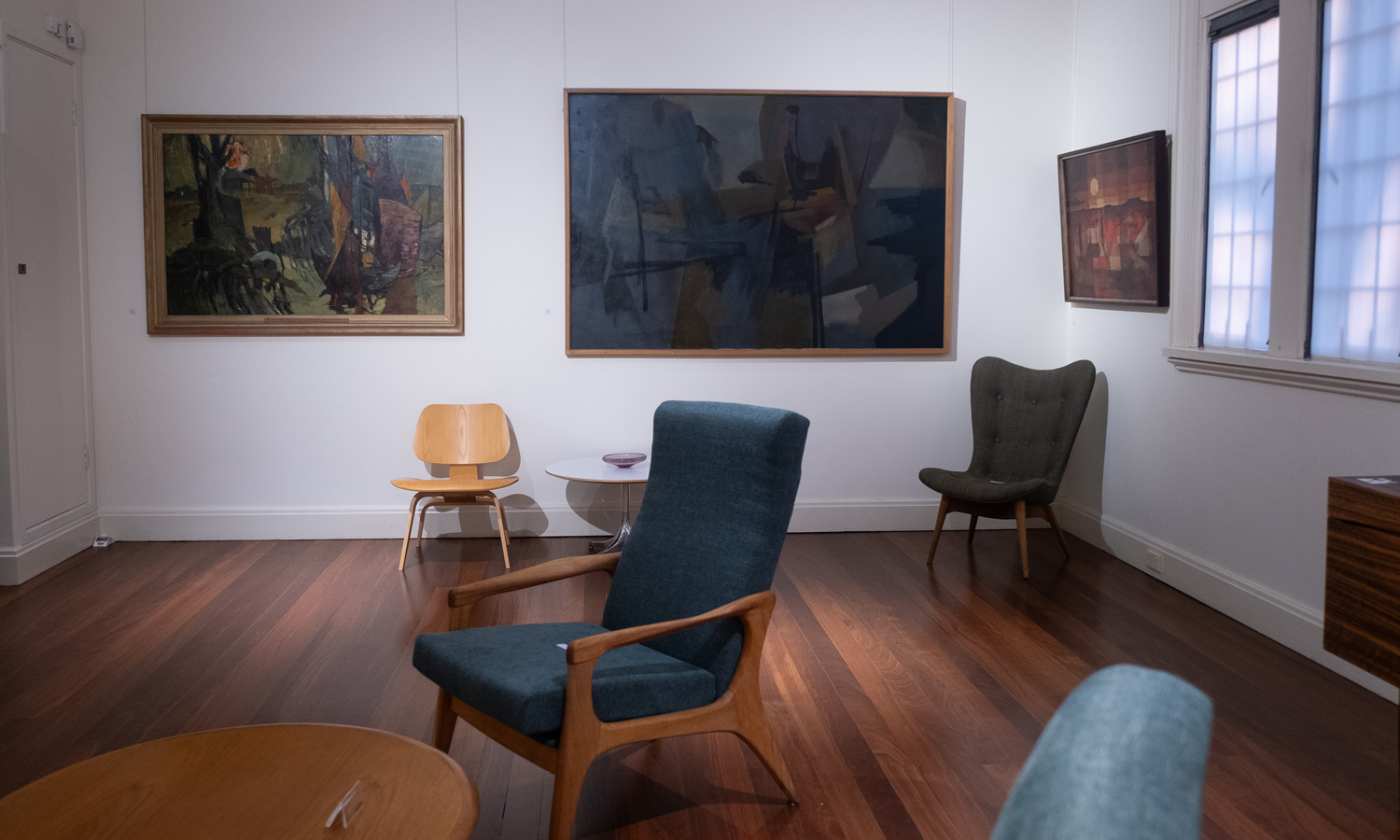 An installation image of 'Adelaide Mid-Century Moderns', which includes mid-20th-century modern furniture alongside paintings and prints by 25 Adelaide artists. Photo: Luke Simon Photography / supplied