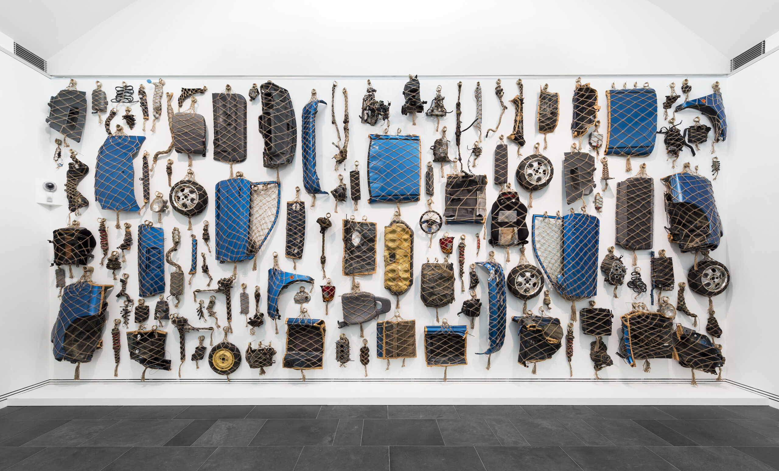 We Hunt Mammoth (2018) by Claire Healy and Sean Cordeiro is a dismantled vehicle, individual parts netted for assembly across an entire wall of the Rockhampton Museum of Art as a tribute to the Mad Max movies.