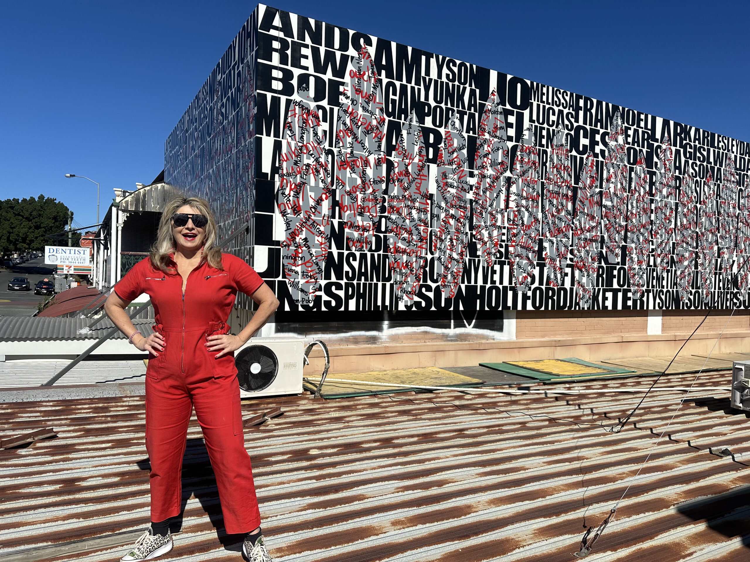 Bec Mac of Chrysalis Projects in front of the stunning Vernon Ah Kee-designed mural Charcoal Stories, atop Avid Reader bookshop in West End.
